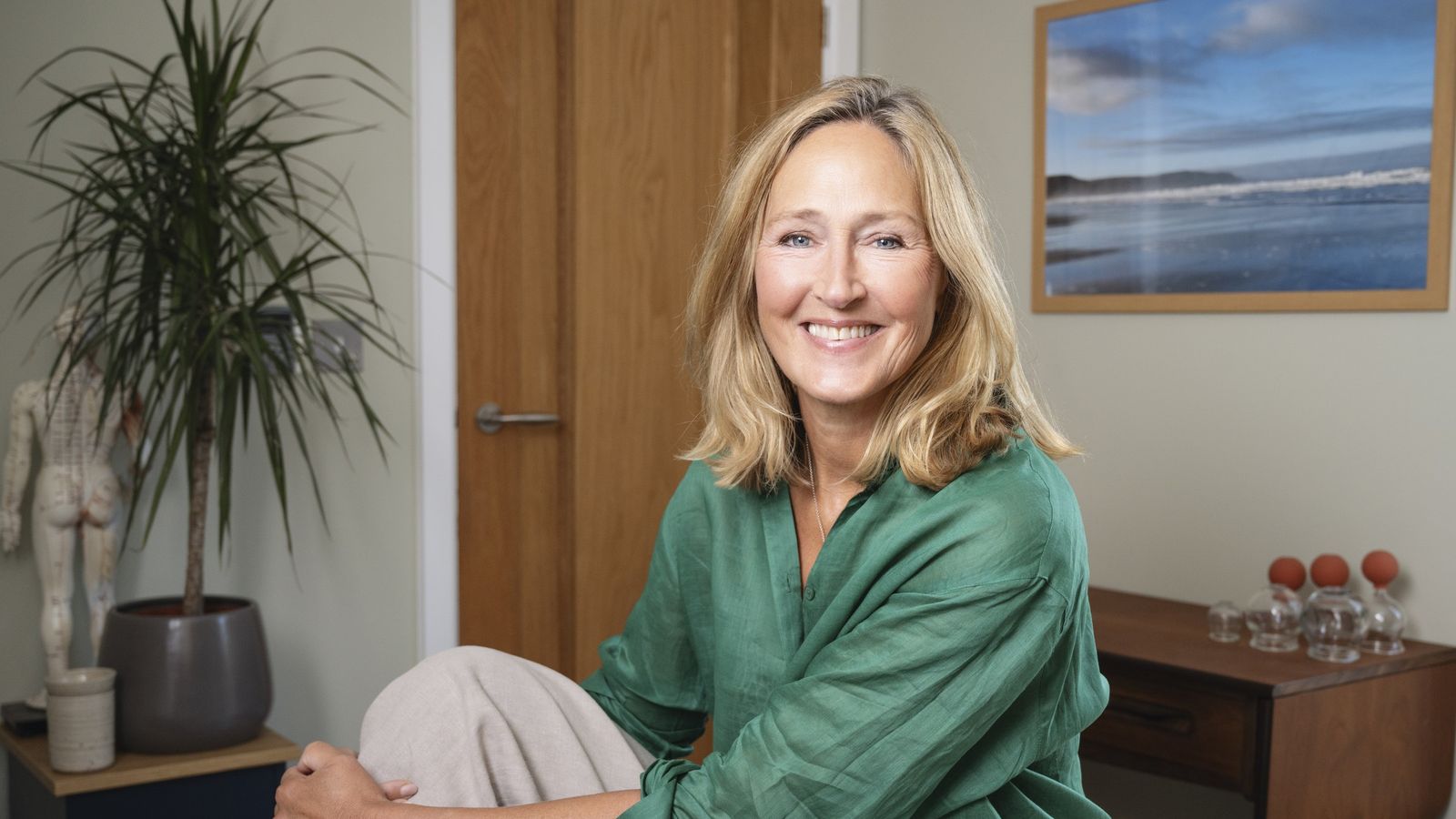 Jac in her treatment room: plants, soft light and a seascape on the wall